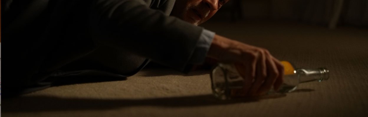 Мужчина лежит на полу и тянется за бутылкой